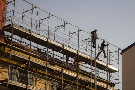 evocative image of workers engaged in assembling a scaffolding for a building to be restructuredの写真素材