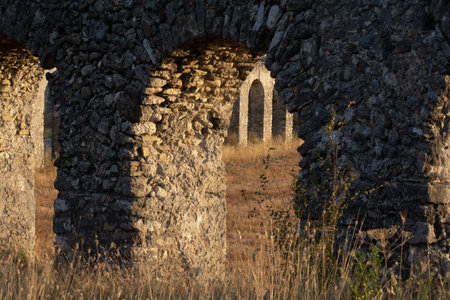 A breathtaking sunset casts a warm, golden hue over the ancient ruins of the Roman aqueduct. The weathered stone arches stand tall, silhouetted against the colorful sky, evoking a sense of history and timeless beauty.の写真素材