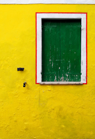 A yellow wall with a wooden green window surrounded by a frame の写真素材