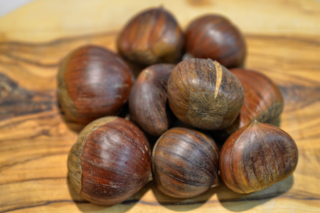 A wooden chopping board with a group of chestnuts looking full and rich, ready to be engraved and cooked.の写真素材
