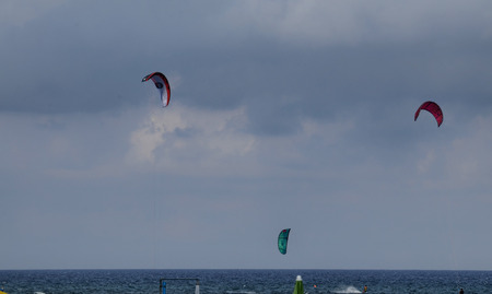 Albenga, Liguria, Italy. July 2018. Kitesurfing on the sea of Albenga, the brightly colored sails enliven the blue sky. On the surface of the water the trails of the boards whizzing past the sail.のeditorial素材