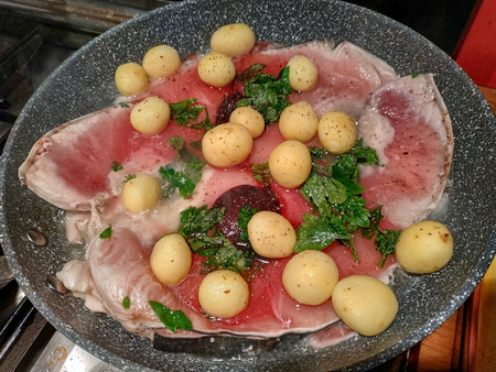 Pan cooking slices of swordfish, seasoned with fresh parsley leaves, new potatoes, pepper. The cooking moves the slices, a bit of steam rises from the pan.の写真素材