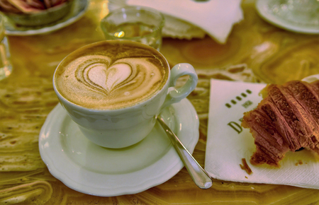 Italian cappuccino and croissants: creamy milk foam and coffee on the surface with a beautiful heart designed playing with the mixture of milk and coffee and a delicious croissant besideのeditorial素材