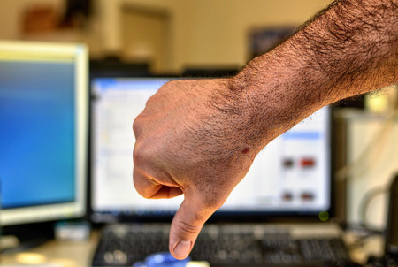 Male hand of Caucasian man makes thumbs down gesture. Indistinguishable blurred background of an office.の写真素材