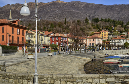 Mergozzo, Piedmont, Italy. March 2019. On the lakefront the houses with warm and bright colors face. Tourists stroll around enjoying the atmosphere, some stop on a bench. Moored boats.のeditorial素材