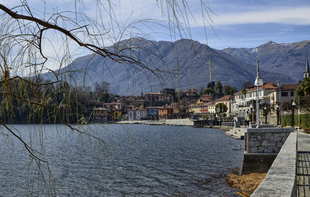 Mergozzo, Piedmont, Italy. March 2019. Pleasant panoramic view of the town overlooking the lake. The fronds of a tree frame the imageのeditorial素材