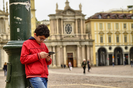 Turin, Piedmont, Italy. April 2019. In Piazza San Carlo people a child consults his smartphone. In the background the twin churches that characterize the place together with the equestrian statueのeditorial素材