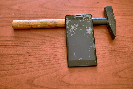 A smartphone with a broken screen and a thousand cracks with a hammer next to itの写真素材