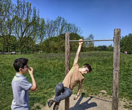 A young and friendly Caucasian boy tries his hand at pulling up the bar, raising himself with a...