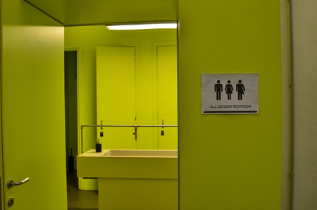 Toilet signage of all kinds next to a bathroom door in acid green with icons of the man, the woman, the transgender. Black icons on a white background.のeditorial素材