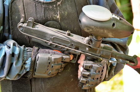 Paintball battle. Detail of the rifle held by a player: you can see the hands with protective gloves and the tank of paint bullets on the top of the rifle.の写真素材