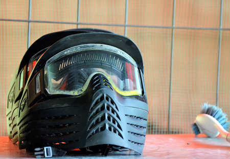 Paintball equipment. A protective helmet, complete with a mask to protect the face, ready to be worn for battle. Next to the brush to remove paint residues.の写真素材