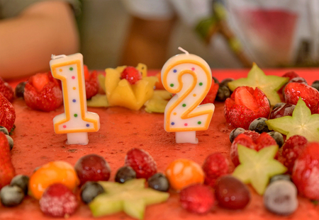 Appetizing fruit ice-cream cake decorated with strawberries, blueberries, cigliege, calamodino, kumquat, apple stars. 1 and 2 shaped candles for a 12 year birthday.の写真素材