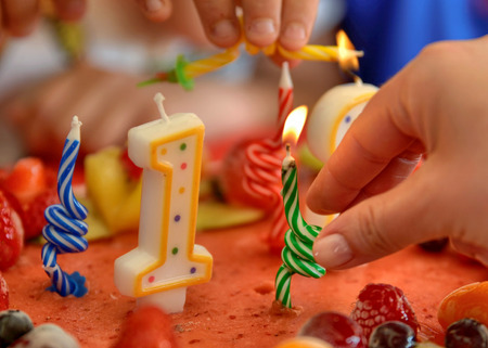 Appetizing fruit ice-cream cake decorated with strawberries, blueberries, cigliege, calamodino, kumquat, apple stars. 1 and 2 shaped candles for a 12 year birthday. Hands position and light them.の写真素材