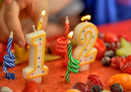 Appetizing fruit ice-cream cake decorated with strawberries, blueberries, cigliege, calamodino, kumquat, apple stars. 1 and 2 shaped candles for a 12 year birthday. Hands position and light them.の写真素材