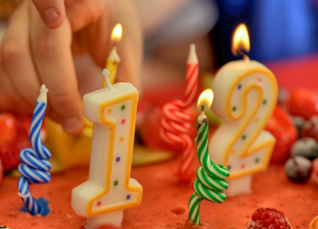 Appetizing fruit ice-cream cake decorated with strawberries, blueberries, cigliege, calamodino, kumquat, apple stars. 1 and 2 shaped candles for a 12 year birthday. Hands position and light them.の写真素材