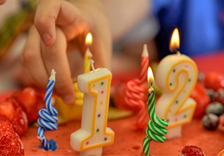 Appetizing fruit ice-cream cake decorated with strawberries, blueberries, cigliege, calamodino, kumquat, apple stars. 1 and 2 shaped candles for a 12 year birthday. Hands position and light them.の写真素材
