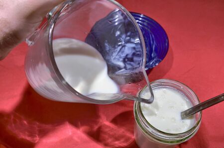 Preparation of Kefir, the glass jar with the granules is filled with milk pouring it from the glass jug.の写真素材