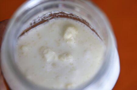 Close-up shot of a glass jar filled with fermenting kefir: the yellowish-white polysaccharisic grains can be seen on the surface of the milk.の写真素材