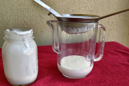Pouring of Kefir, the glass jar is placed next to the net to pour the contents.の写真素材
