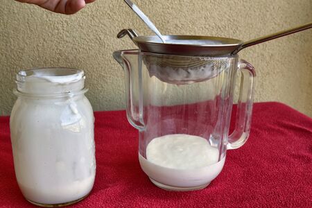 Pouring of Kefir, the glass jar is placed next to the net to pour the contents.の写真素材