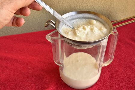 Pouring of the Kefir, the hand of a Caucasian man gently moves the granules in the sieve with a...