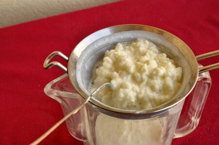 Pouring of the Kefir, the hand of a Caucasian man gently moves the granules in the sieve with a spoon to separate them from the fermented milk.の写真素材