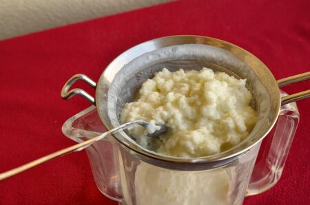 Pouring of the Kefir, the hand of a Caucasian man gently moves the granules in the sieve with a spoon to separate them from the fermented milk.の写真素材