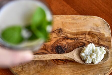 Close-up blurred shot of a glass full of kefir with mint leaves, a wooden spoon full of Kefir granules in the clear backgroundの写真素材