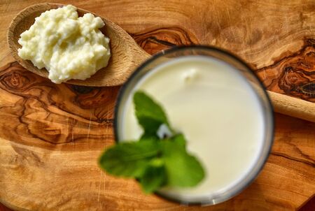 Close-up shot on a full glass of white Kefir enriched with some mint leaves. On the cutting board a wooden spoon full of Kefir ferments.の写真素材