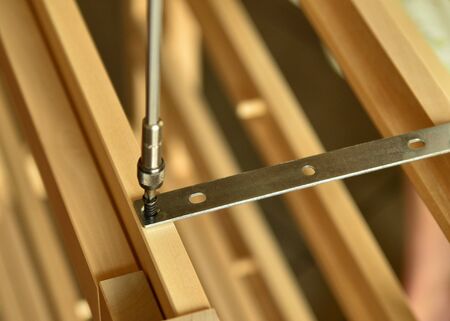 Close-up shot of a pair of screws that is fixed with an electric screwdriver on a light wooden...