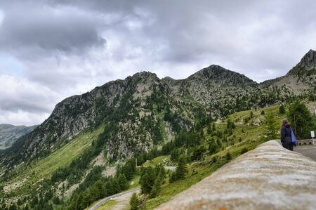 Vinadio, Piedmont, Italy. July 2019. In the province of Cuneo, the sanctuary of Sant'Anna di Vinadio. A woman meditates looking at the valley in front of the sanctuary. Rainy day.の写真素材