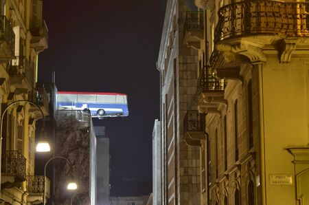 Turin, Piemonte, Italy. November 2019. A bus poised on the roof of a building. You can see the bus swinging slowly. It is an artistic installation in homage to the movie The Italian Job. Night shot.のeditorial素材