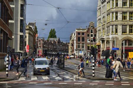 Amsterdam, Holland. August 2019. A road junction in the center: the typical houses, cars, bikes, pedestrians, tram rails coexist. The red asphalt reserved for bikes stands out.のeditorial素材