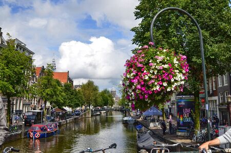 Amsterdam, Holland. August 2019. Enchanting view of one of the canals of the historic center from a bridge. The brightly colored flowers frame the amazing view.のeditorial素材