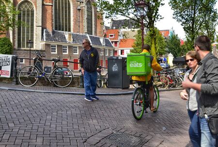 Amsterdam, Holland. August 2019. In the red-light district the old church is a landmark. An uber eats worker goes around with his bike to make a delivery.のeditorial素材