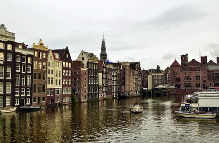 Amsterdam, Holland, August 2019. At the beginning of the Damrak, the typical Dutch houses overlook the water. The boats are moored on the moorings.のeditorial素材