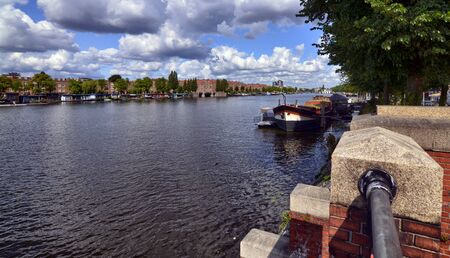 Amsterdam, Holland, August 2019. View of the Amstel River, outskirts of the city. A large moored boat is used as a houseboat. Sunny day with blue sky and white clouds.のeditorial素材