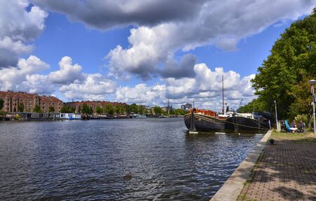 Amsterdam, Holland, August 2019. View of the Amstel River, outskirts of the city. A large moored boat is used as a houseboat. Sunny day with blue sky and white clouds.のeditorial素材
