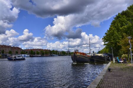 Amsterdam, Holland, August 2019. View of the Amstel River, outskirts of the city. A large moored boat is used as a houseboat. Sunny day with blue sky and white clouds.のeditorial素材