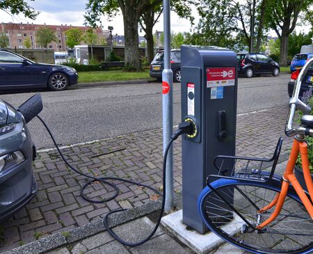 Amsterdam, Holland, August 2019. Along the Amstel river, an electric car is being charged: the cable with the connector connected on the nose of the car starts from the charging column.のeditorial素材