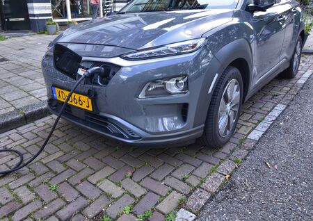 Amsterdam, Holland, August 2019. Along the Amstel river, an electric car is being charged: the cable with the connector connected on the nose of the car starts from the charging column.のeditorial素材