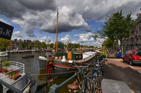 Amsterdam, Holland, August 2019. View of the Amstel River, outskirts of the city. A large moored boat is used as a houseboat. Sunny day with blue sky and white clouds.のeditorial素材