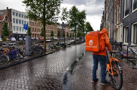 Amsterdam, Holland, August 2019. A worker from Thuisbezorgd, home delivery company for food and drink. It is easy to notice them: the showy the orange bag with the white writing.のeditorial素材