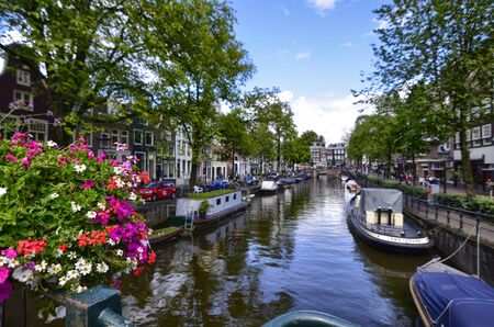 Amsterdam,Holland,August 2019. Enchanting view of a canals of the historic center. The typical houses overlook the water, boats moored along the canal. Planters on railings and bikes. Sunny day.のeditorial素材