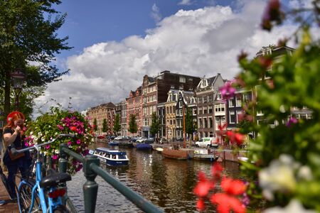 Amsterdam,Holland,August 2019. Enchanting view of a canals of the historic center. The typical houses overlook the water, boats moored along the canal. Planters on railings and bikes. Sunny day.のeditorial素材