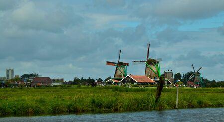 Zaanse Schans, Holland, August 2019. North-east of Amsterdam is a small community located on the quay of the Zaan river. View from above of the fields with mills, tourists are noticed. Cloudy day.のeditorial素材