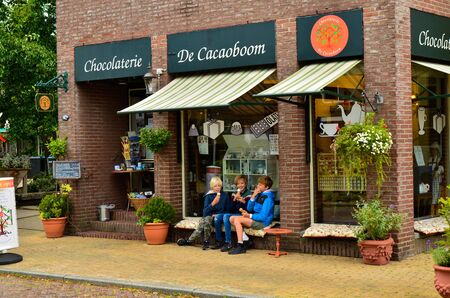 Zaandijk, Holland, August 2019. Northeast Amsterdam is a small community located on the Zaan River. Three kids enjoy an ice cream on the shop bench. Red brick facade.のeditorial素材
