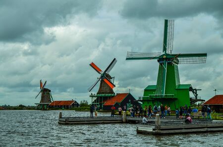 Zaanse Schans, Holland, August 2019. Northeast Amsterdam is a small community located on the Zaan River. View of the mills on the river bank, they stand out with their bright colors. Cloudy day.のeditorial素材