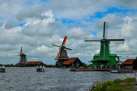Zaanse Schans, Holland, August 2019. Northeast Amsterdam is a small community located on the Zaan River. View of the mills on the river bank, they stand out with their bright colors. Cloudy day.のeditorial素材